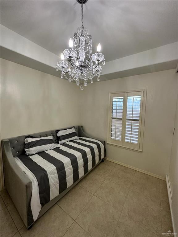 tiled bedroom with a raised ceiling, a chandelier, and baseboards