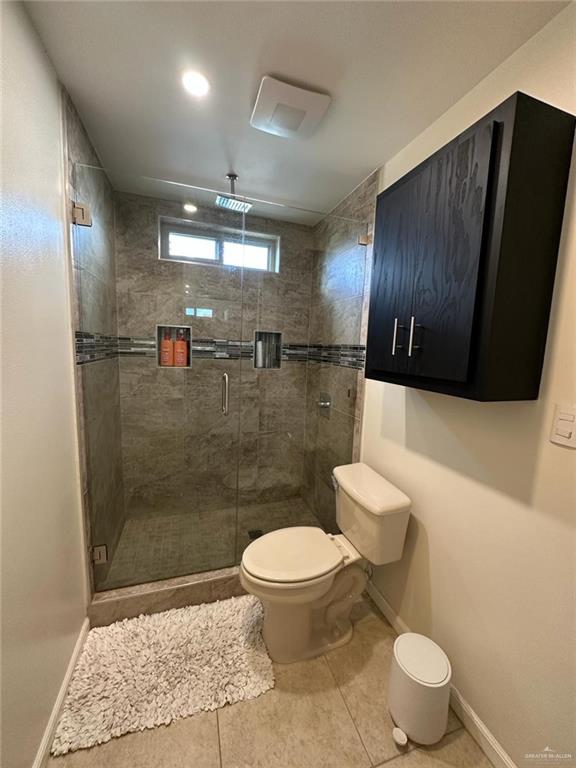 bathroom featuring toilet, a shower stall, tile patterned floors, and baseboards