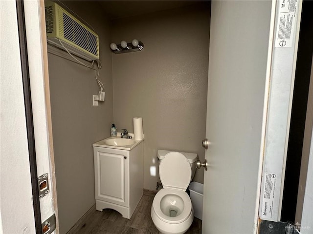 half bath featuring toilet, vanity, a wall unit AC, and wood finished floors