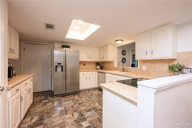 2405 E Lazy Lake Dr, Harlingen, TX 78550 - kitchen featuring stainless steel appliances, a skylight, tile countertops, a sink, and white cabinets