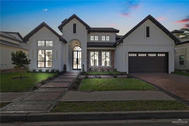 view of front of house with decorative driveway, a yard, and stucco siding