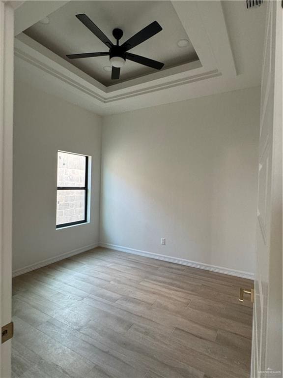 spare room with a raised ceiling, ceiling fan, and light hardwood / wood-style flooring