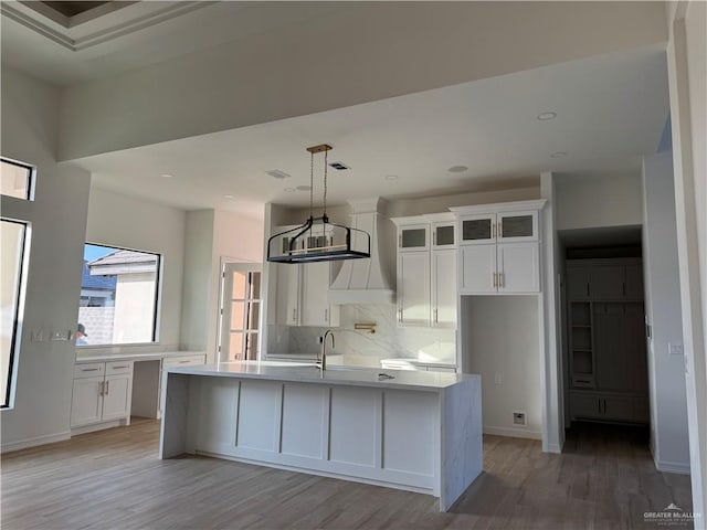 kitchen featuring tasteful backsplash, light hardwood / wood-style flooring, decorative light fixtures, a kitchen island with sink, and white cabinets