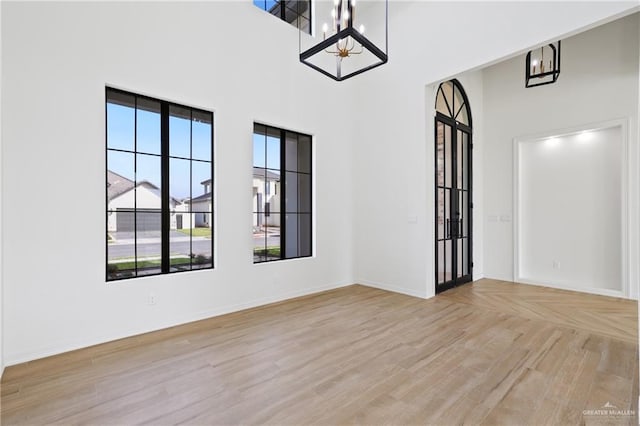 empty room with a notable chandelier, baseboards, light wood-style floors, and a towering ceiling