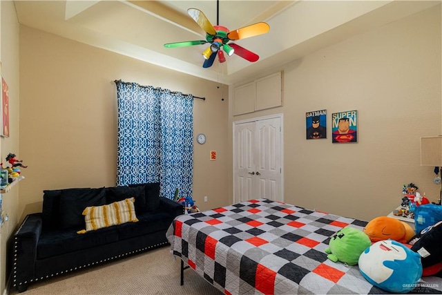 carpeted bedroom featuring a raised ceiling, ceiling fan, and a closet