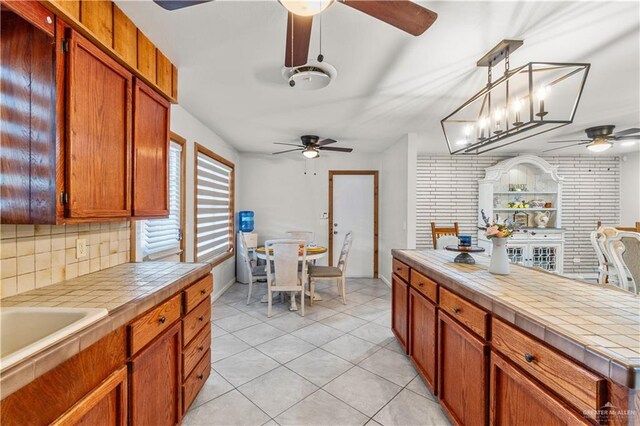18064 Garrett Rd, Harlingen, TX 78552 - kitchen with ceiling fan, tile countertops, tasteful backsplash, light tile patterned floors, and brown cabinetry