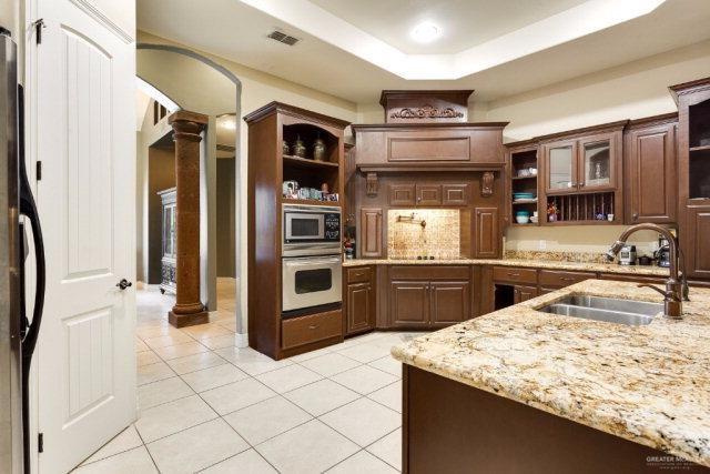 kitchen featuring ornate columns, dark brown cabinetry, stainless steel appliances, a raised ceiling, and sink