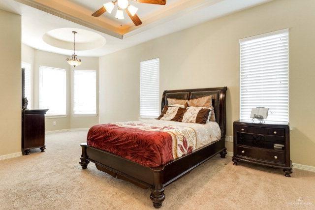 carpeted bedroom with ceiling fan and a raised ceiling