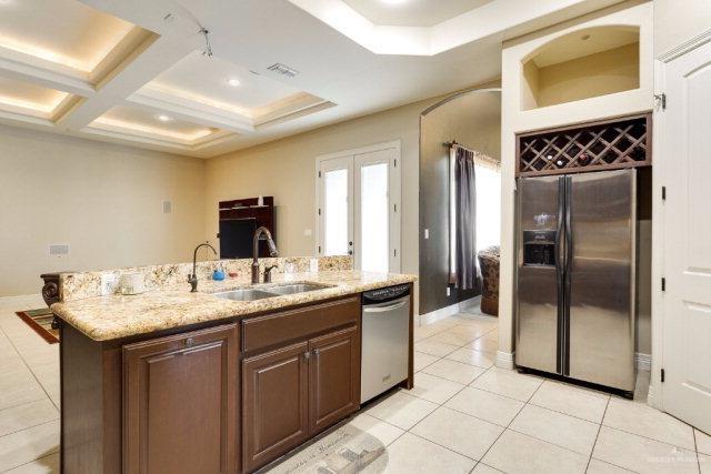 kitchen with coffered ceiling, stainless steel appliances, sink, an island with sink, and light tile patterned flooring