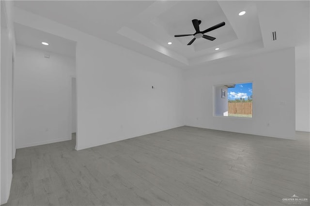 empty room featuring ceiling fan, visible vents, a raised ceiling, and wood finished floors