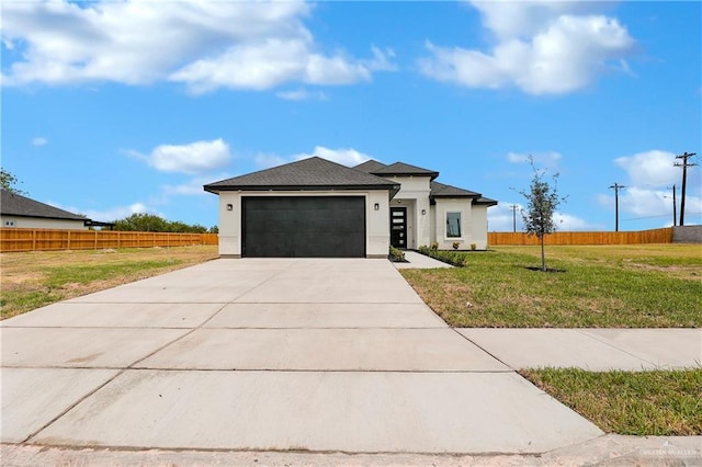 prairie-style house with a front lawn, fence, concrete driveway, stucco siding, and an attached garage