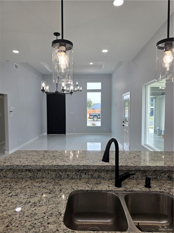 kitchen with an inviting chandelier, light stone counters, hanging light fixtures, and sink