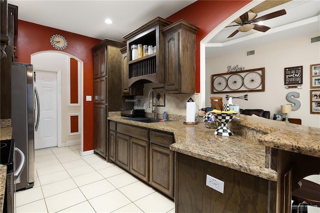 kitchen featuring sink, ceiling fan, light stone countertops, light tile patterned flooring, and dark brown cabinetry