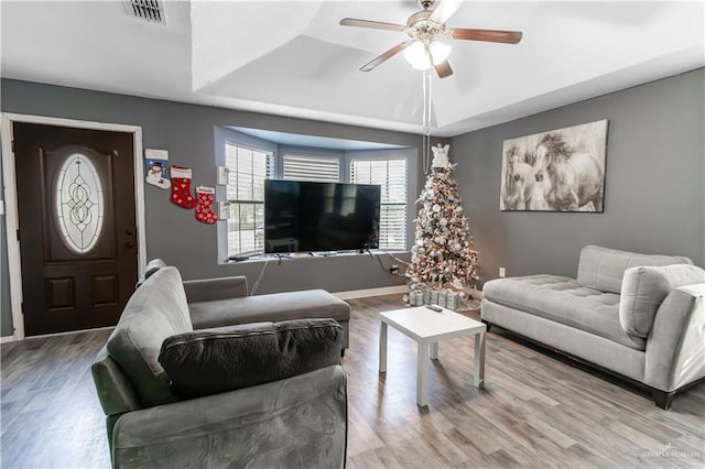 living room featuring a tray ceiling, ceiling fan, and light hardwood / wood-style floors