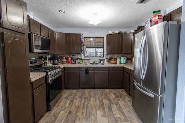 kitchen with hardwood / wood-style floors, dark brown cabinets, a textured ceiling, and appliances with stainless steel finishes