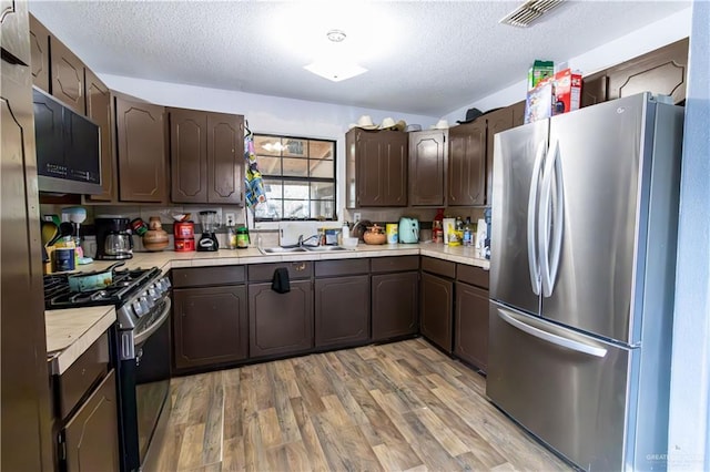 kitchen featuring a textured ceiling, dark brown cabinetry, stainless steel appliances, and sink