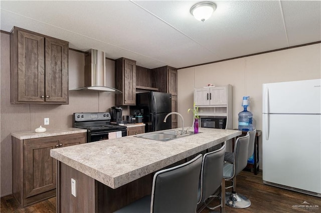 kitchen with light countertops, a breakfast bar area, a sink, black appliances, and wall chimney exhaust hood