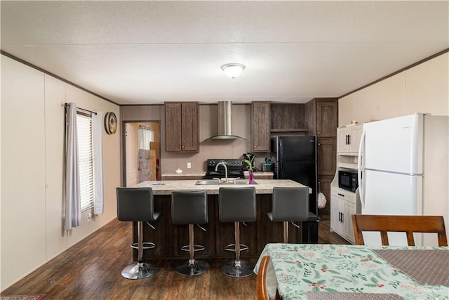kitchen featuring an island with sink, light countertops, wall chimney exhaust hood, black appliances, and dark wood-type flooring