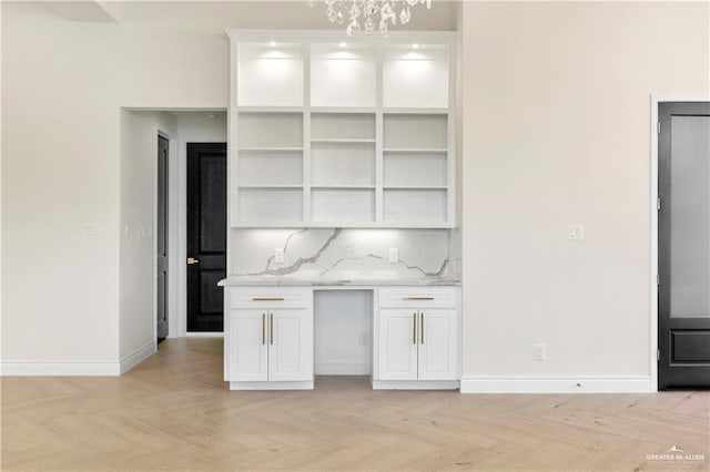 kitchen featuring tasteful backsplash, light stone counters, a notable chandelier, white cabinets, and light parquet flooring