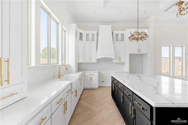 kitchen featuring a center island, sink, custom range hood, decorative light fixtures, and white cabinetry