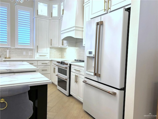 kitchen with premium range hood, light hardwood / wood-style flooring, tasteful backsplash, white cabinetry, and stainless steel appliances