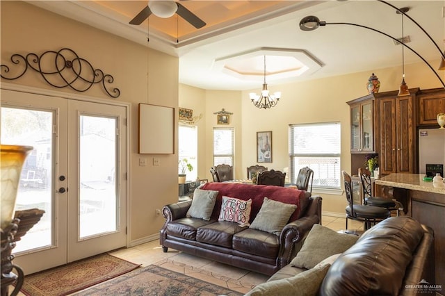 tiled living room with french doors, a raised ceiling, and an inviting chandelier