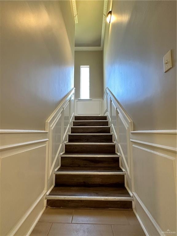 stairway featuring a wainscoted wall, crown molding, a decorative wall, and tile patterned floors