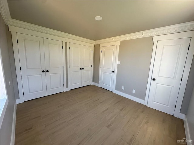 unfurnished bedroom featuring light wood-style floors, baseboards, and two closets