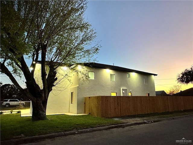 property exterior at dusk with a yard, fence, and stucco siding