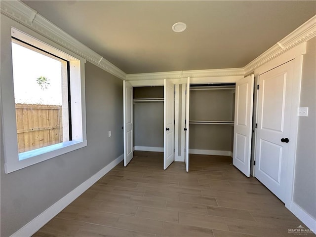 unfurnished bedroom with crown molding, light wood-style floors, two closets, and baseboards