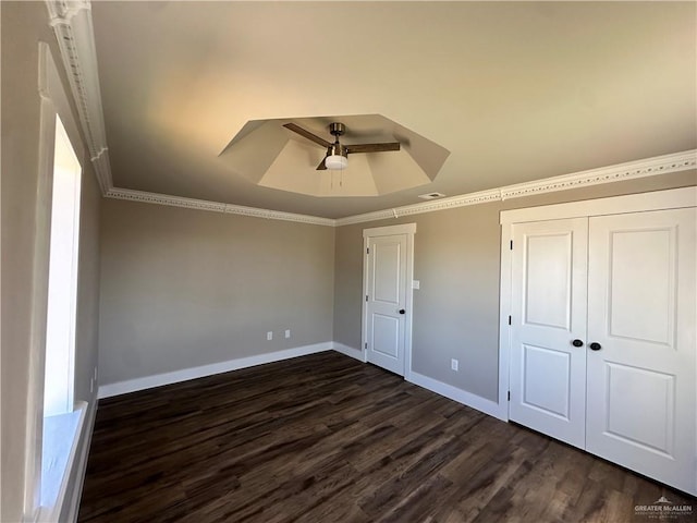 unfurnished bedroom featuring crown molding, baseboards, a raised ceiling, and dark wood finished floors