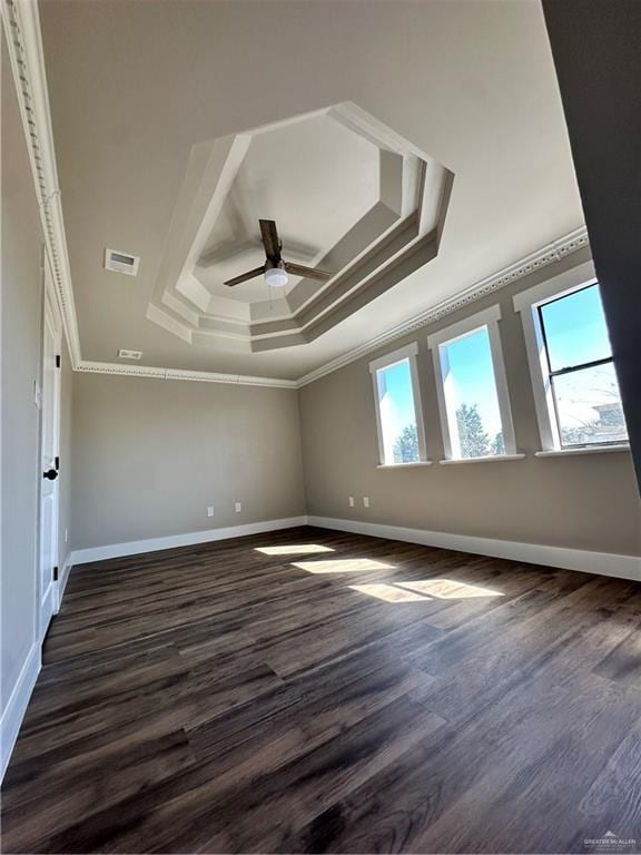 unfurnished room with visible vents, a tray ceiling, dark wood-type flooring, and crown molding