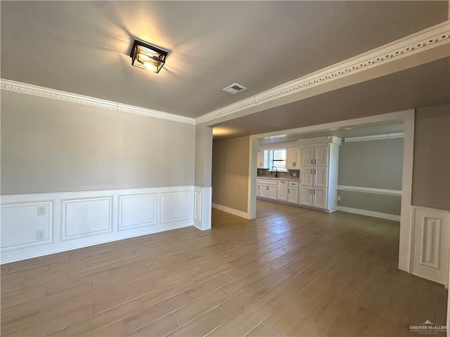 unfurnished room with light wood-style flooring, a decorative wall, a wainscoted wall, visible vents, and crown molding