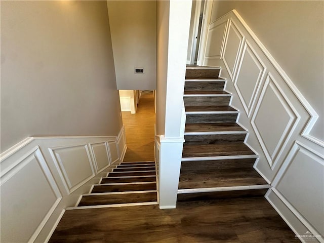 stairs with a wainscoted wall, wood finished floors, and a decorative wall