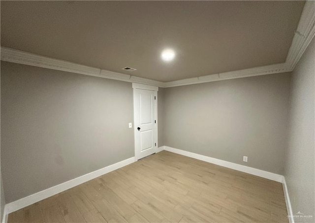 spare room with light wood finished floors, baseboards, visible vents, and crown molding