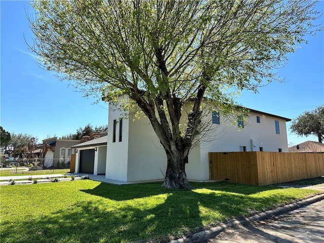 view of side of property featuring a lawn, an attached garage, fence, and stucco siding