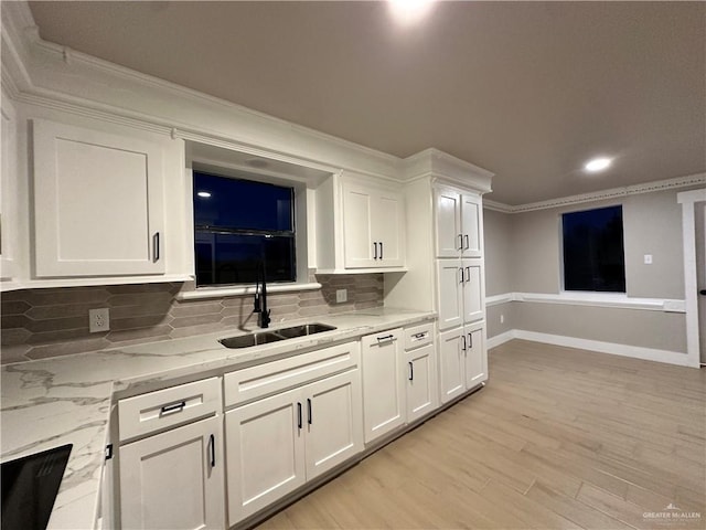 kitchen with crown molding, a sink, white cabinetry, and light stone countertops