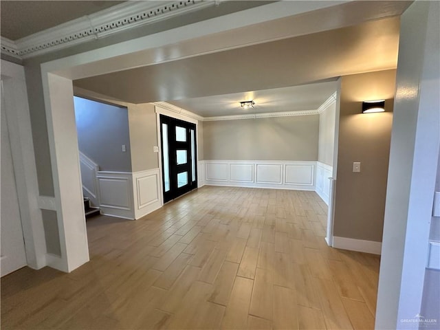 foyer entrance with a wainscoted wall, crown molding, light wood finished floors, a decorative wall, and stairs