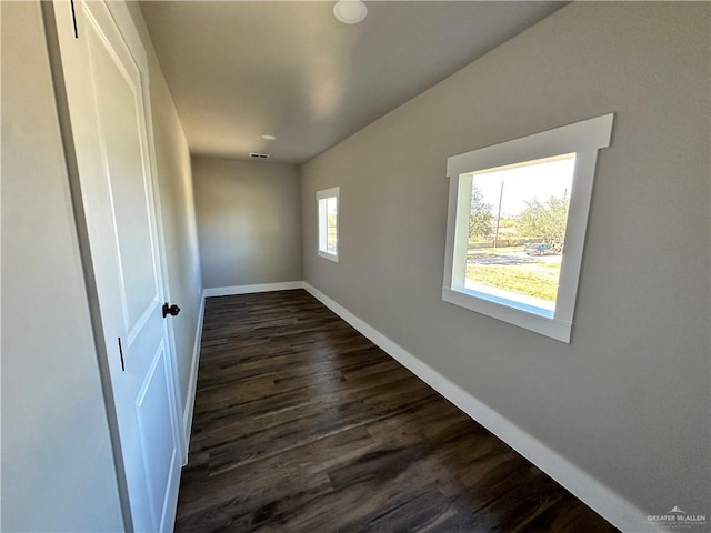 empty room featuring dark wood-style flooring, visible vents, and baseboards