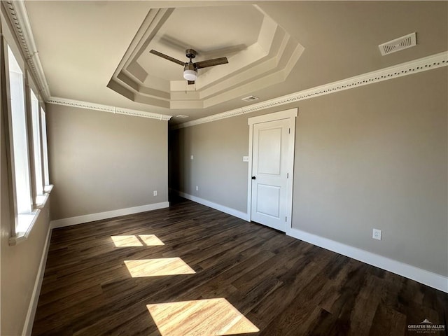 unfurnished bedroom featuring dark wood-style floors, crown molding, a raised ceiling, visible vents, and baseboards