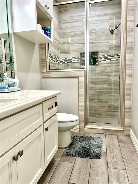 bathroom featuring toilet, a shower with shower door, and vanity