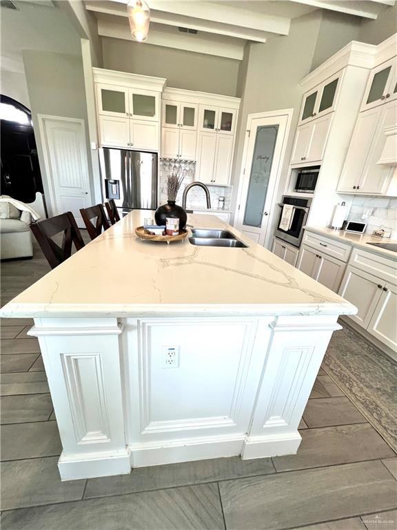 kitchen featuring beam ceiling, a breakfast bar, sink, an island with sink, and stainless steel appliances