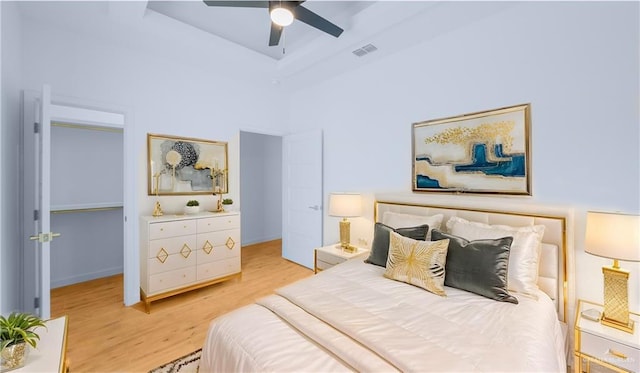bedroom with visible vents, a walk in closet, a raised ceiling, a ceiling fan, and light wood-style flooring