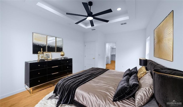 bedroom featuring a raised ceiling, light wood-style floors, recessed lighting, baseboards, and visible vents