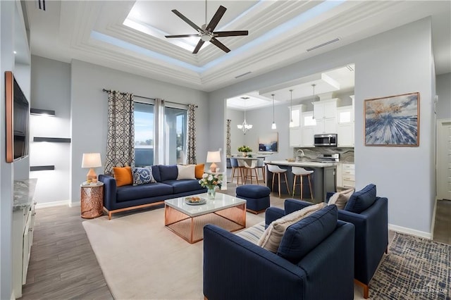 living room with ceiling fan with notable chandelier, a raised ceiling, dark wood-type flooring, sink, and crown molding