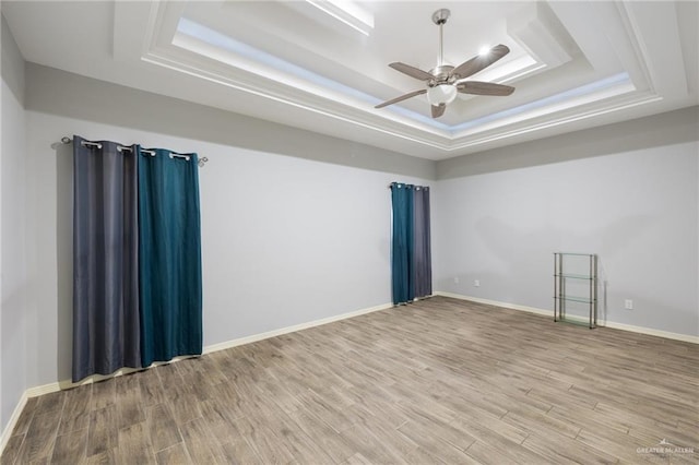 empty room with a raised ceiling, ceiling fan, and light hardwood / wood-style flooring