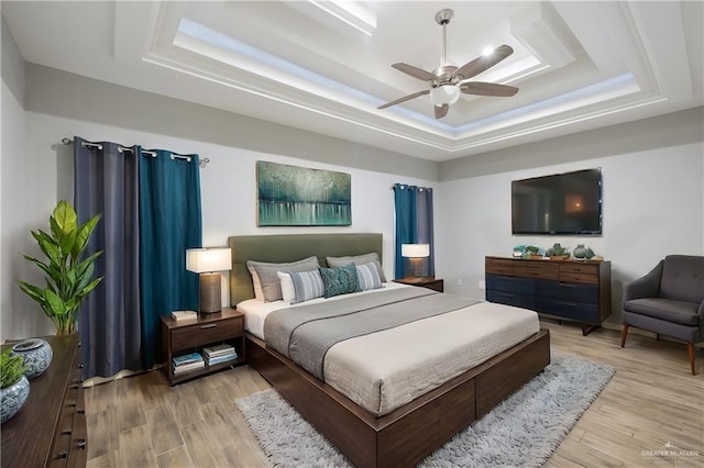 bedroom featuring ceiling fan, light hardwood / wood-style floors, and a tray ceiling