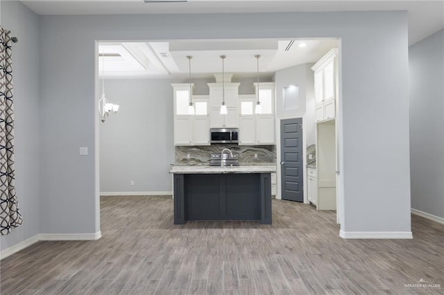 kitchen featuring hanging light fixtures, light hardwood / wood-style flooring, an island with sink, decorative backsplash, and white cabinets