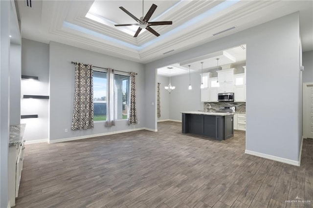 kitchen featuring a raised ceiling, decorative light fixtures, a center island with sink, white cabinets, and appliances with stainless steel finishes