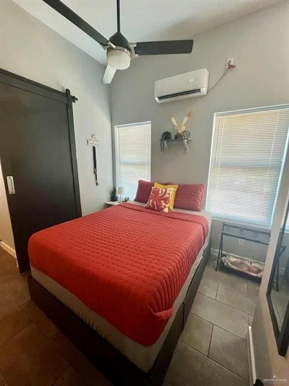 tiled bedroom with ceiling fan, a barn door, a wall unit AC, and baseboards